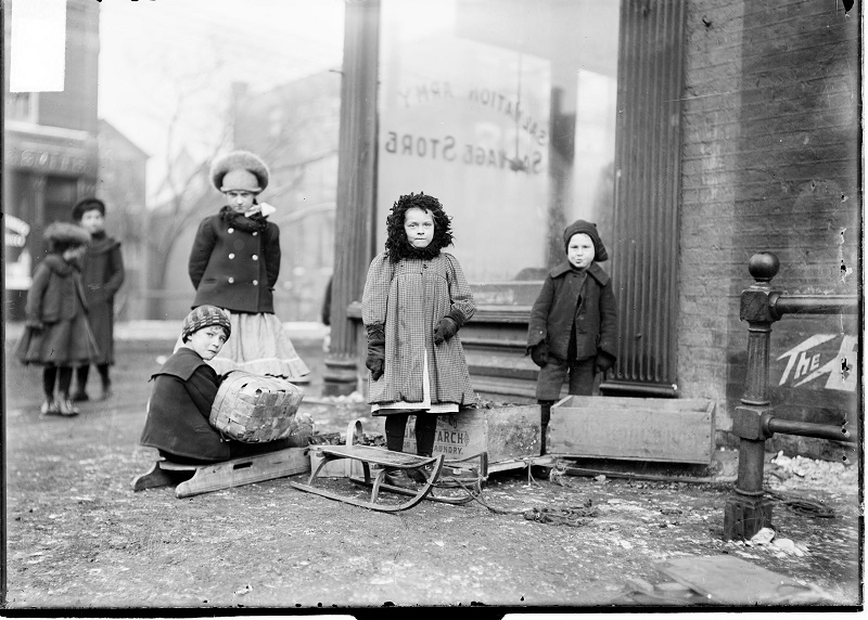Children with sleds and boxes on a street corner by the Salvation Army salvage store. Image of a group of children with sleds and boxes on a street corner by the Salvation Army salvage store in Chicago, Illinois, where coal was distributed to the poor at cost. Source: DN-0000496, Chicago Daily News negatives collection, Chicago History Museum. Date: ca. 1903.