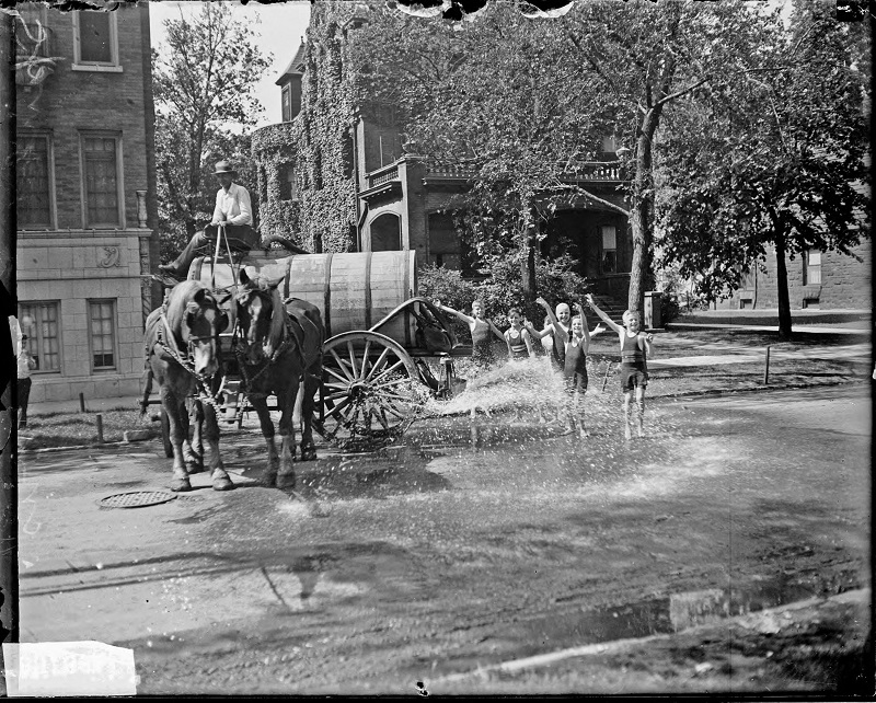Children standing in a sprinkler attached to a horse-drawn wagon on a street. Informal full-length portrait of children wearing bathing suits, standing in a sprinkler attached to a horse-drawn wagon on a street in Chicago, Illinois. Source: DN-0083661, Chicago Daily News negatives collection, Chicago Historical Society. Date: 1927.